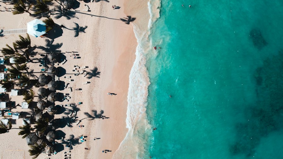 Vista aérea de una playa ancha de arena clara, con gente en la orilla y el mar turquesa.